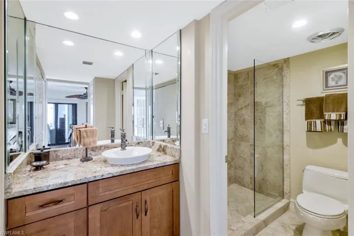 Bathroom featuring ceiling fan, toilet, a shower with door, and vanity