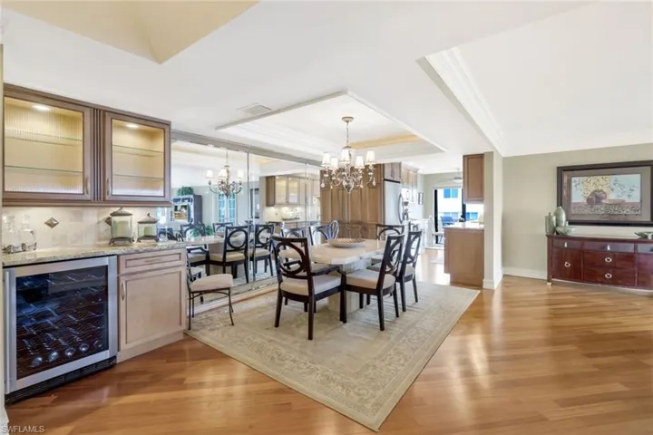 Dining area with an inviting chandelier, crown molding, light hardwood / wood-style floors, a tray ceiling, and beverage cooler