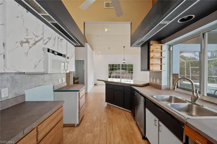 Kitchen featuring hanging light fixtures, light wood-type flooring, healthy amount of natural light, and white microwave