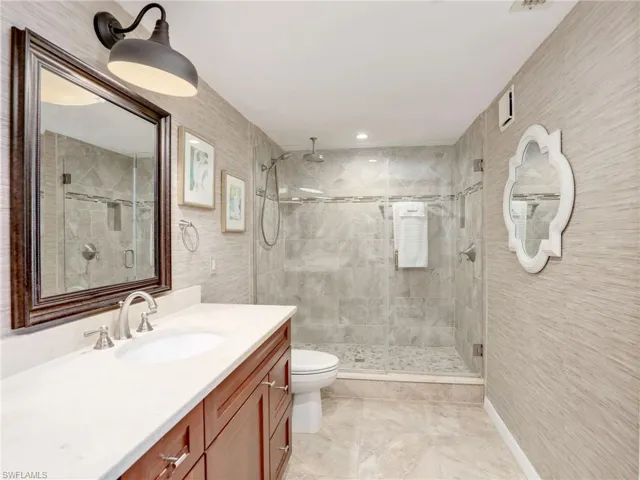 Bathroom with dual vanity, toilet, and a shower with glass door
