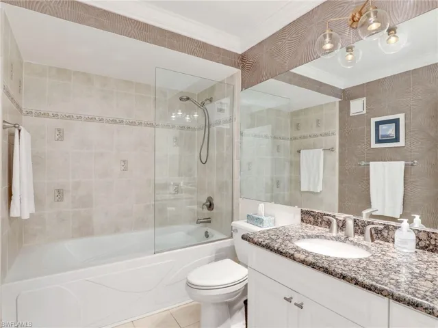 Full bathroom with tile patterned floors, ornamental molding, vanity, tiled shower / bath combo, and toilet