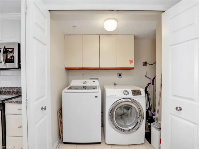 Laundry room with built in cabinets, light tile patterned flooring, a textured ceiling, and washer and clothes dryer