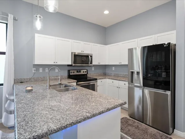 Kitchen featuring stainless steel appliances, light stone counters, white cabinets, a peninsula, and a kitchen breakfast bar
