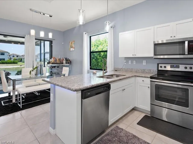 Kitchen featuring appliances with stainless steel finishes, white cabinetry, light tile patterned floors, and a peninsula