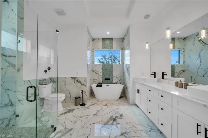 Bathroom with plenty of natural light, a freestanding bath, double vanity, a marble finish shower, and recessed lighting