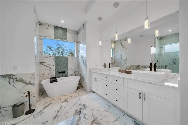 Full bathroom featuring double vanity, stone wall, a freestanding bath, and recessed lighting