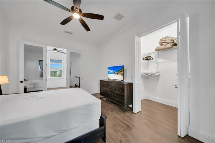 Bedroom with crown molding, wood finished floors, a walk in closet, and ceiling fan