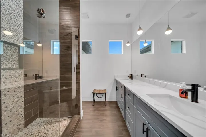 Bathroom with double vanity, tiled shower, and dark wood-type flooring