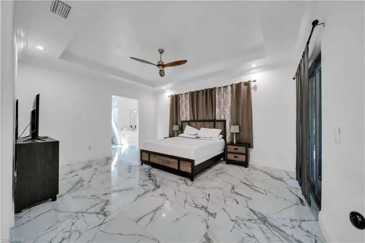 Bedroom featuring a ceiling fan, recessed lighting, light marble finish flooring, and connected bathroom