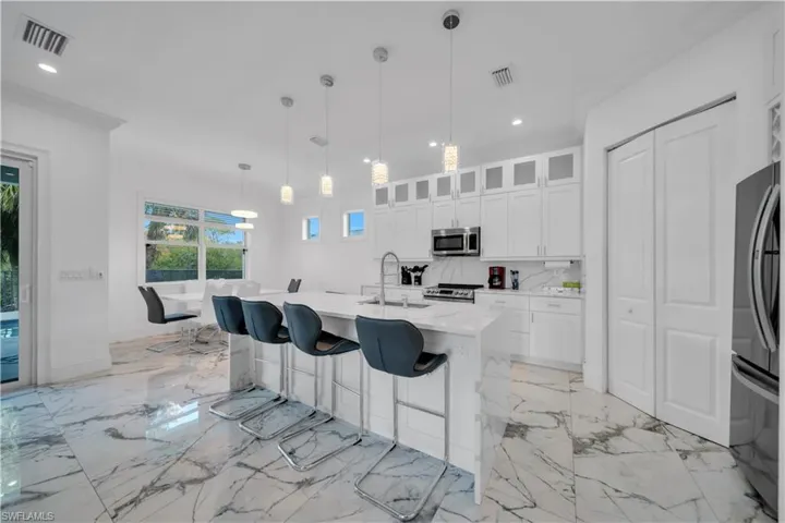 Kitchen featuring glass fronted cabinets, a kitchen bar, light stone countertops, pendant lighting, and white cabinetry