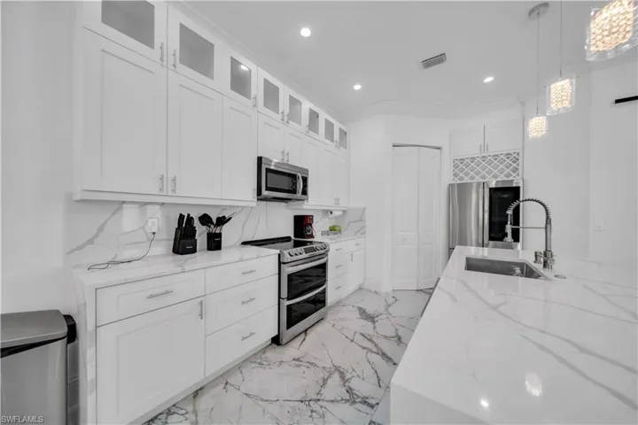 Kitchen with light stone counters, glass insert cabinets, stainless steel appliances, decorative light fixtures, and white cabinetry