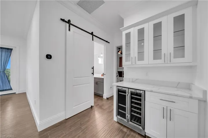 Bar area featuring white cabinets, a barn door, light stone counters, crown molding, and wine cooler