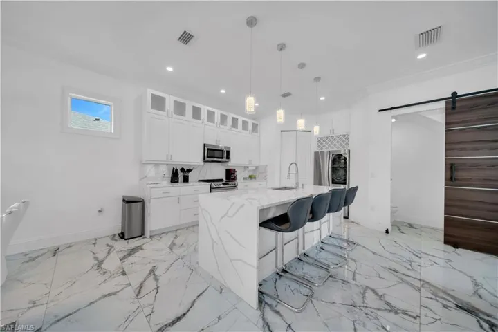 Kitchen with a barn door, a kitchen breakfast bar, light stone counters, decorative light fixtures, and white cabinetry