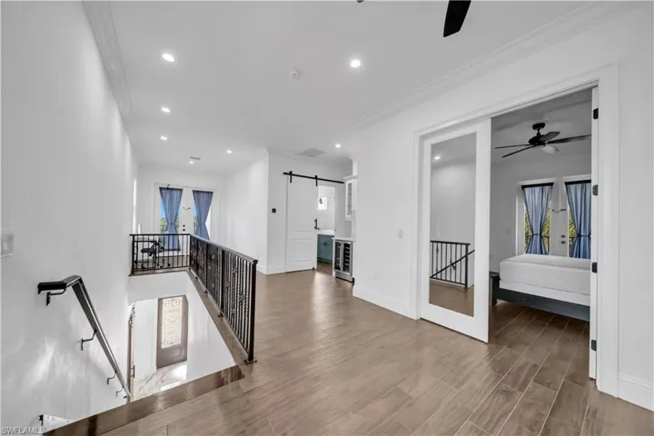 Hallway with an upstairs landing, crown molding, wood tiled floors, recessed lighting, and a barn door