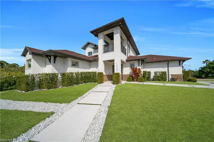 View of front of home featuring stucco siding, a balcony, a front yard, and stone siding