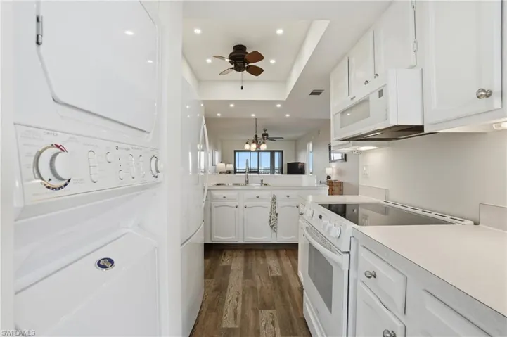 Kitchen featuring white stove/microwave, white cabinetry, light countertops,, and a ceiling fan , in unit stackable washer/dryer- Virtually Edited Image