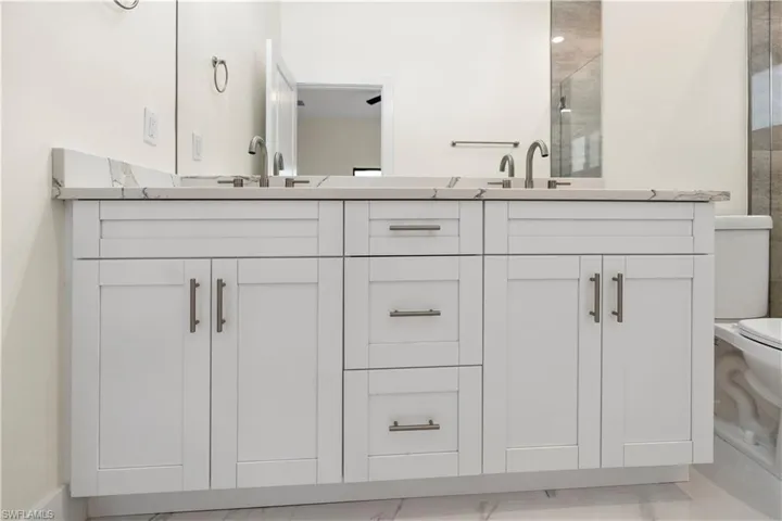 Bathroom with double vanity, a stall shower, and light marble finish floors