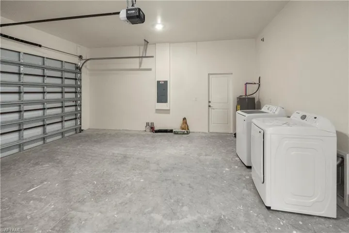 Garage with washer and dryer, electric panel, a garage door opener, and water heater