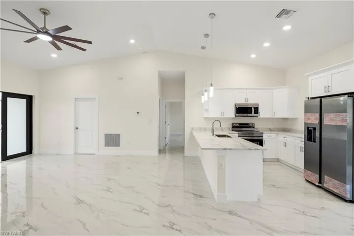 Kitchen with appliances with stainless steel finishes, hanging light fixtures, white cabinetry, a peninsula, and open floor plan