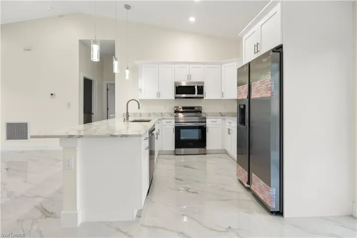 Kitchen featuring appliances with stainless steel finishes, white cabinets, decorative light fixtures, a peninsula, and high vaulted ceiling