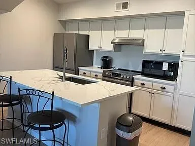 Kitchen with a kitchen bar, a kitchen island with sink, white cabinetry, and freestanding refrigerator