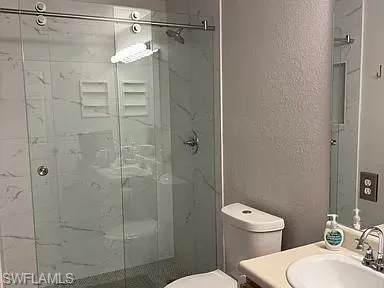 Bathroom with a marble finish shower, a textured wall, and vanity