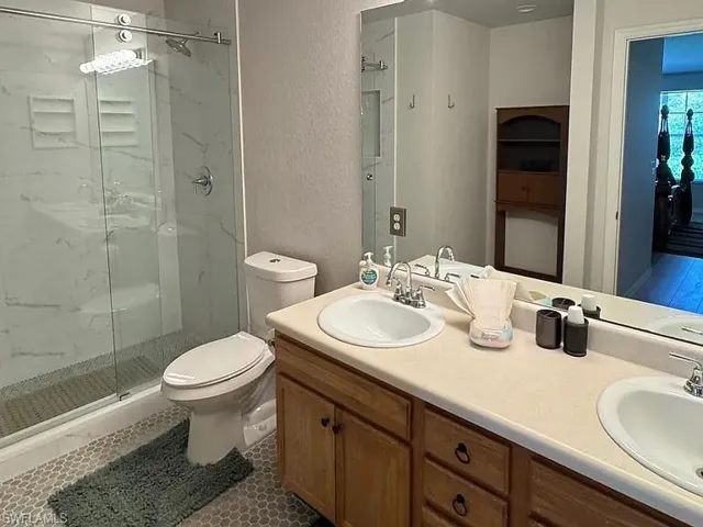 Full bath with a marble finish shower, double vanity, a textured wall, and dark tile patterned flooring