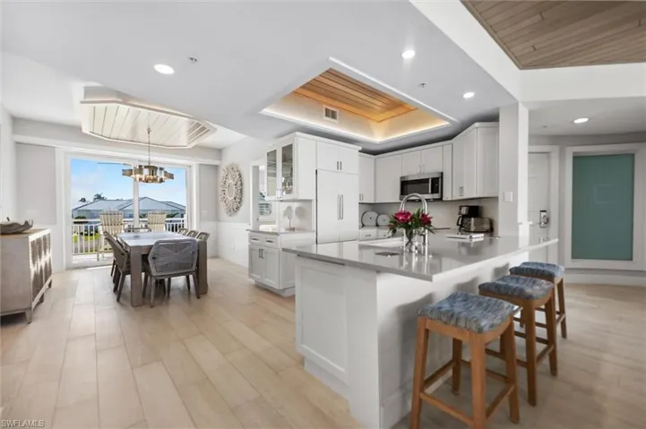 Kitchen with a wood tray ceiling, a kitchen breakfast bar, glass fronted cabinets, white cabinetry, and stainless steel microwave