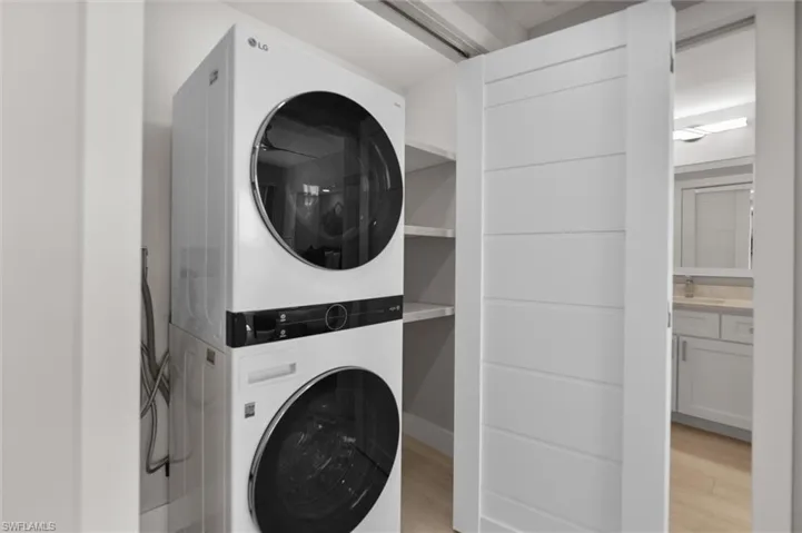 Laundry area featuring stacked washer and clothes dryer and light wood finished floors