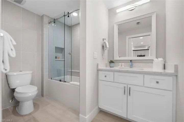 Bathroom with vanity, shower / bath combination with glass door, tile walls, and light wood-style floors