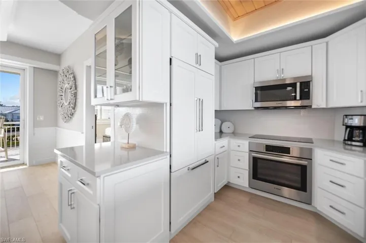 Kitchen with glass insert cabinets, stainless steel appliances, white cabinetry, a wainscoted wall, and light stone countertops