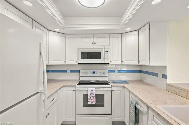Kitchen with white appliances, recessed lighting, white cabinetry, backsplash, and crown molding