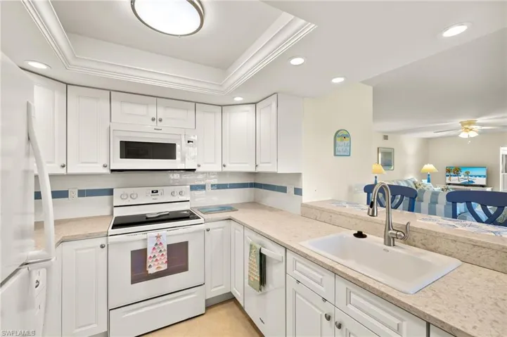 Kitchen with white appliances, recessed lighting, white cabinets, backsplash, and light stone countertops
