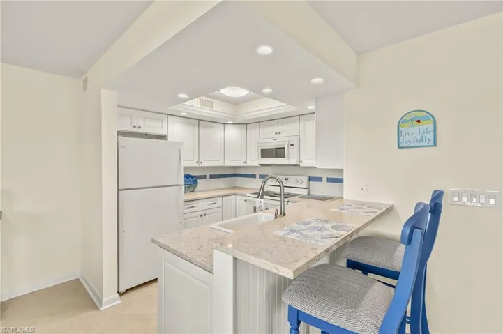 Kitchen featuring white appliances, recessed lighting, white cabinets, a kitchen breakfast bar, and a peninsula