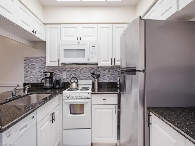 Kitchen with sink, white appliances, dark stone counters, and white cabinets