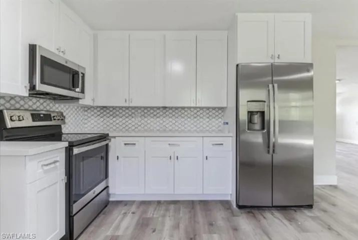Kitchen with backsplash, white cabinets, light hardwood / wood-style floors, and appliances with stainless steel finishes