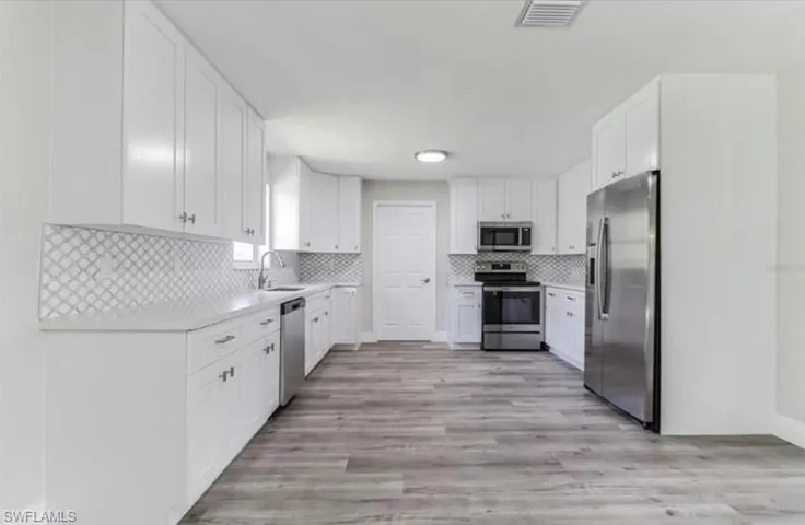 Kitchen featuring sink, appliances with stainless steel finishes, decorative backsplash, white cabinets, and light wood-type flooring
