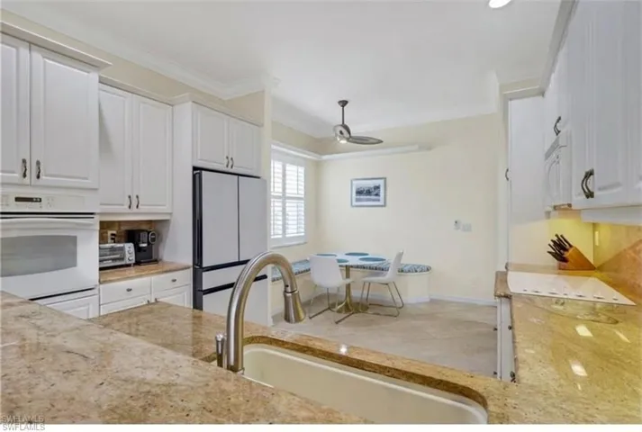 Kitchen featuring white appliances, white cabinets, light stone counters, ornamental molding, and a ceiling fan