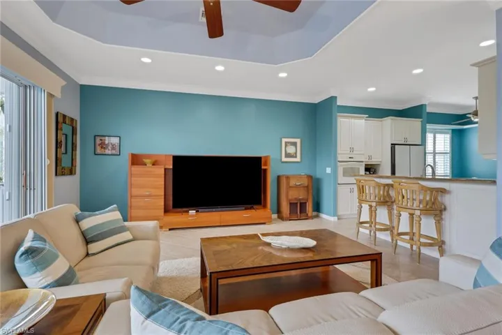 Living area featuring a ceiling fan, crown molding, recessed lighting, light tile patterned flooring, and a tray ceiling