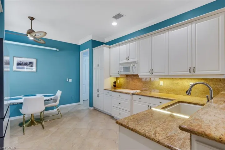 Kitchen with white cabinetry, light stone countertops, white appliances, ornamental molding, and decorative backsplash