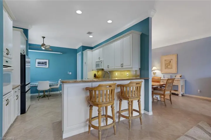 Kitchen featuring a kitchen bar, white cabinetry, light stone counters, a ceiling fan, and backsplash