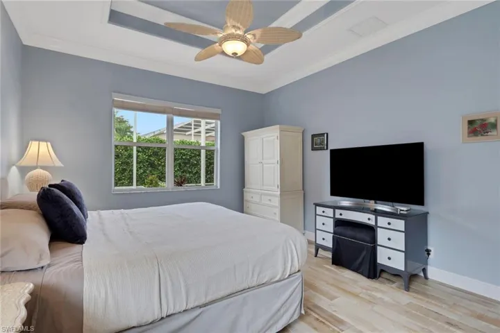 Bedroom featuring light wood-style floors, ornamental molding, a ceiling fan, and a tray ceiling