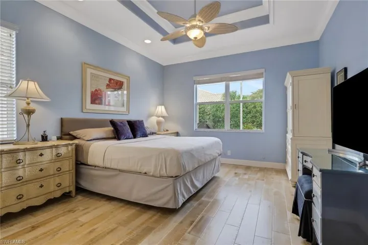 Bedroom with light wood-style flooring, ornamental molding, ceiling fan, recessed lighting, and a raised ceiling