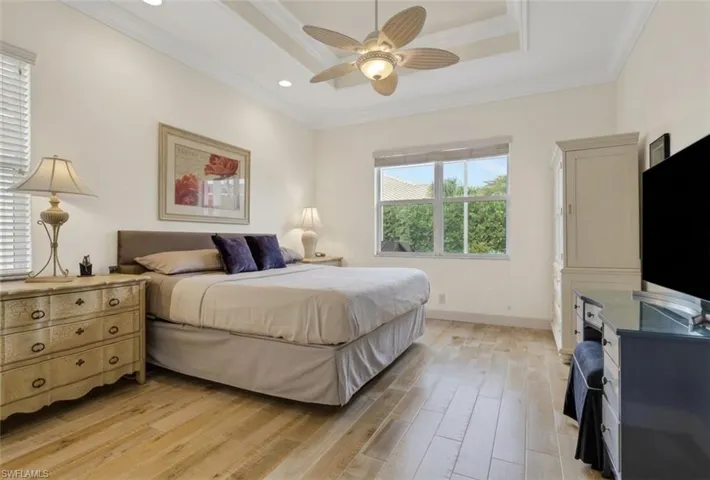 Bedroom featuring crown molding, light wood-style flooring, ceiling fan, and a raised ceiling