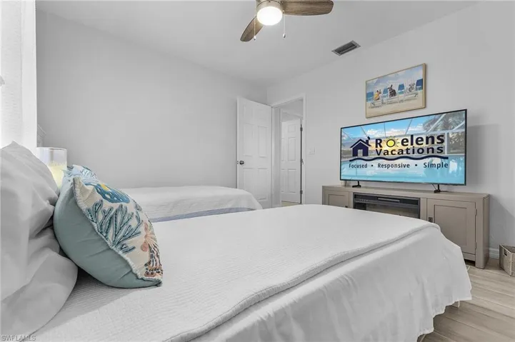 Bedroom with light wood-finish flooring, two beds, and a ceiling fan