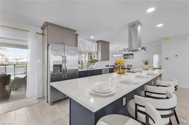 Spacious kitchen featuring a large island with a light-toned countertop, a stainless steel refrigerator, and recessed lighting