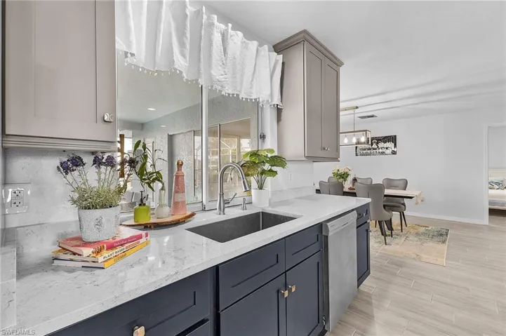 Modern kitchen featuring two-tone cabinetry, a stainless steel sink with a gooseneck faucet, light-toned countertops, and a stainless steel dishwasher