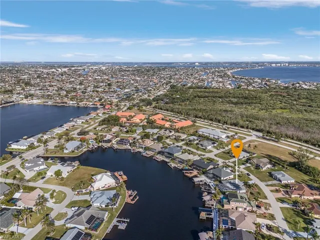 Waterfront property situated on a canal, featuring a paved driveway, mature landscaping, and a dock structure