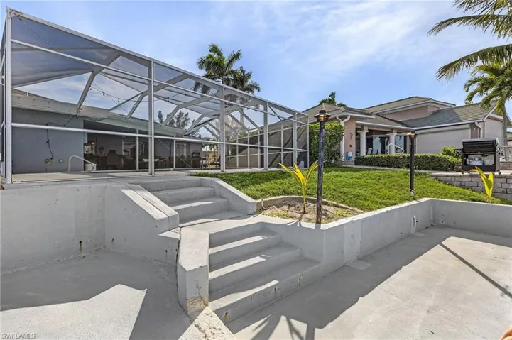 Screened outdoor living area with concrete stairs, featuring a manicured lawn, established landscaping, and a multi-level concrete patio