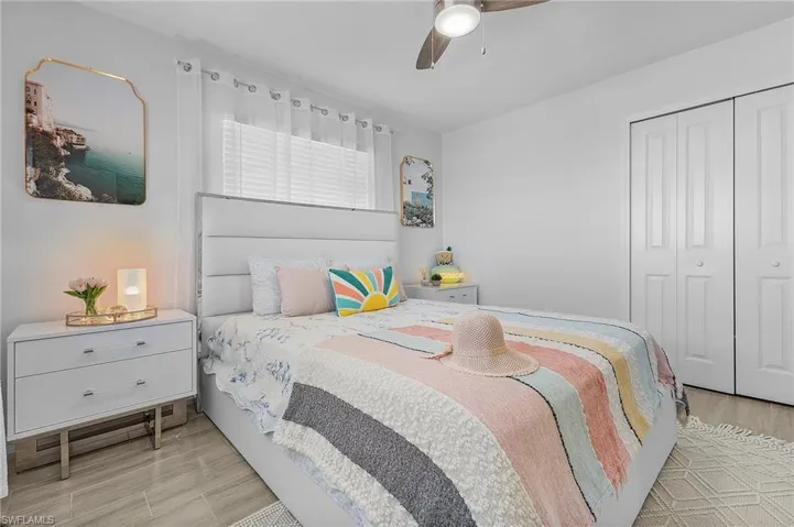Bedroom featuring light wood-finish flooring, a ceiling fan with integrated lighting, window with blinds, and bi-fold closet doors